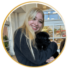 female with long blonde hair holding a small black puppy